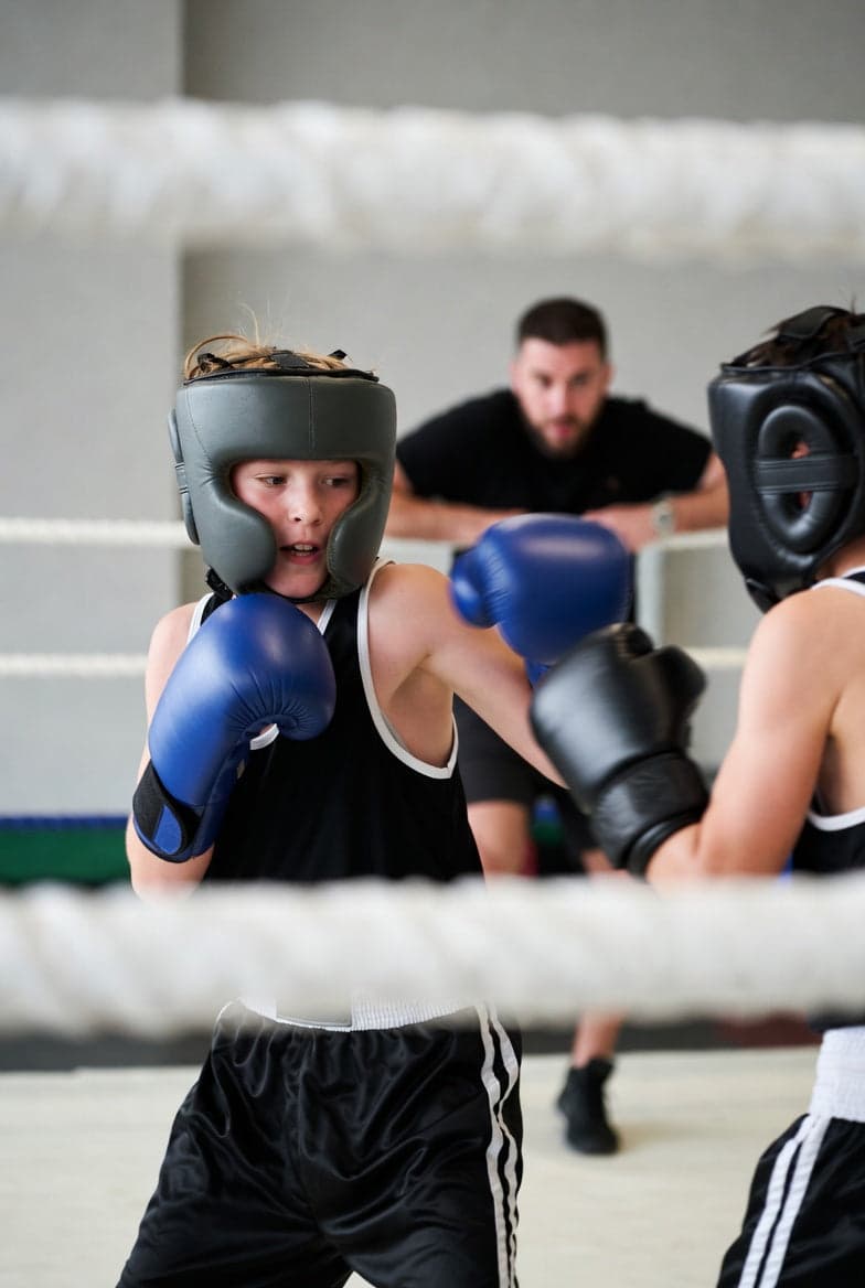 Barn sparrer med hjelm og hansker under oppsyn av trener – kontrollert sparring for barn
